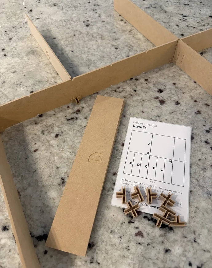 A device partly assembled on a countertop: dividers slotted together, a loose divider, and the joints laid on the order's printed layout sheet