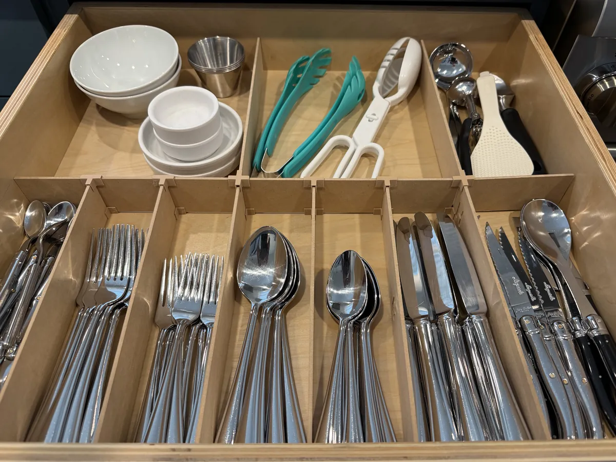 A utensils drawer fitted with an Object Containment Device: bowls and serving tools in the compartments at the back, and cutlery sorted into narrow slots across the front