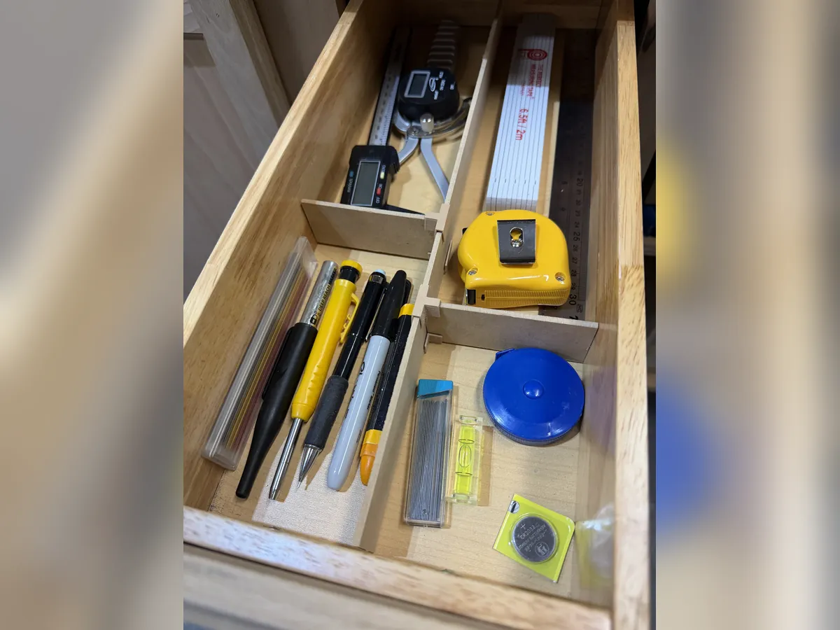 A workshop drawer fitted with an Object Containment Device: pencils and markers, tape measures, a level and a caliper sorted into their own compartments